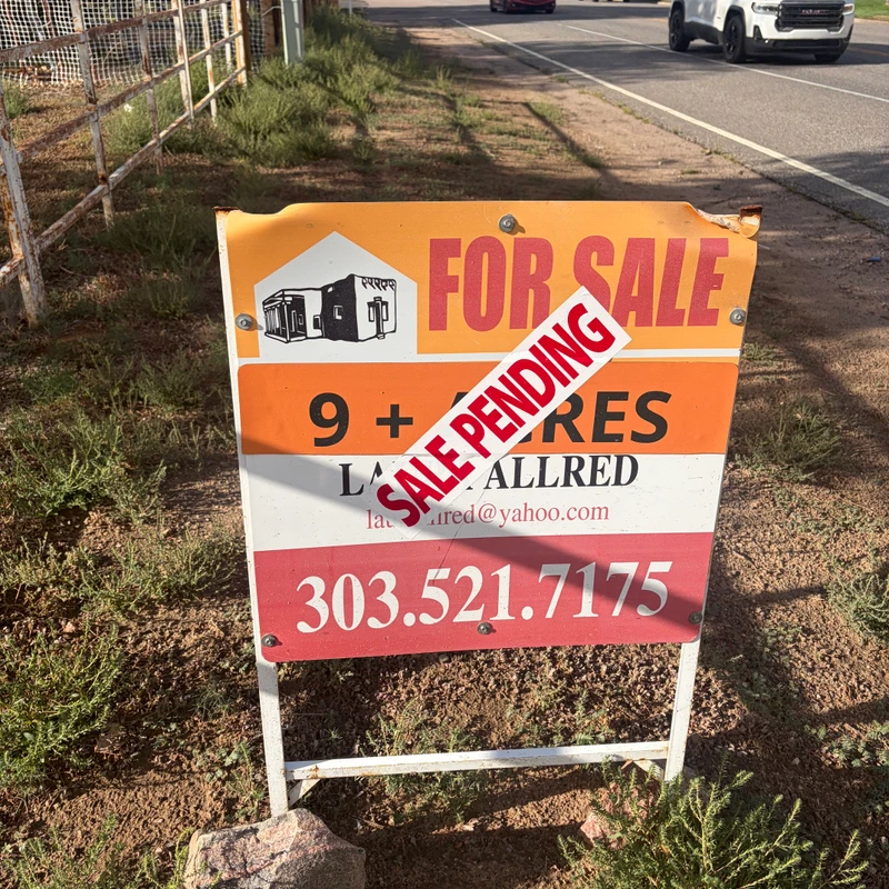 A roadside real estate sign advertises over nine acres of land for sale. A large red and white sticker diagonally across the sign reads 'SALE PENDING'.