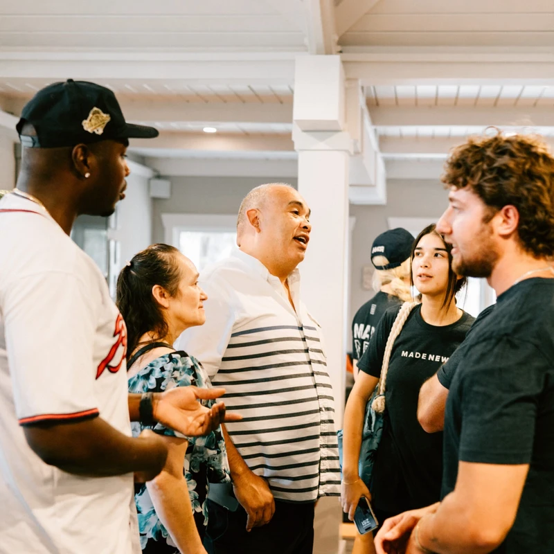 A diverse group of five people stand together indoors, talking and listening intently to each other during a casual social event.