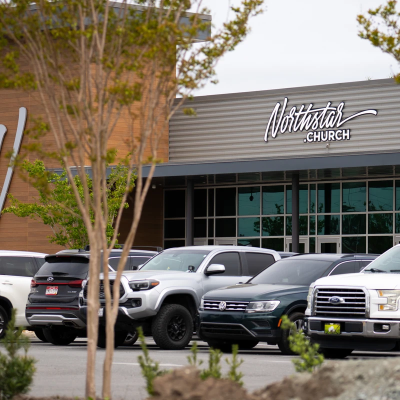 The modern building of Northstar Church, with its name in cursive script, seen from across a parking lot filled with cars and trucks on an overcast day.