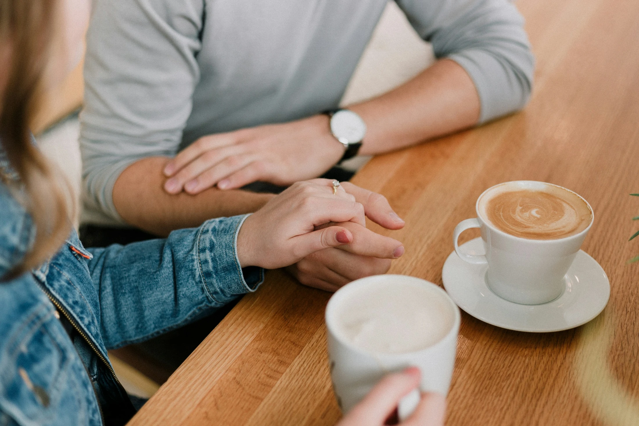 Two people talking over coffee, one hand resting on the other