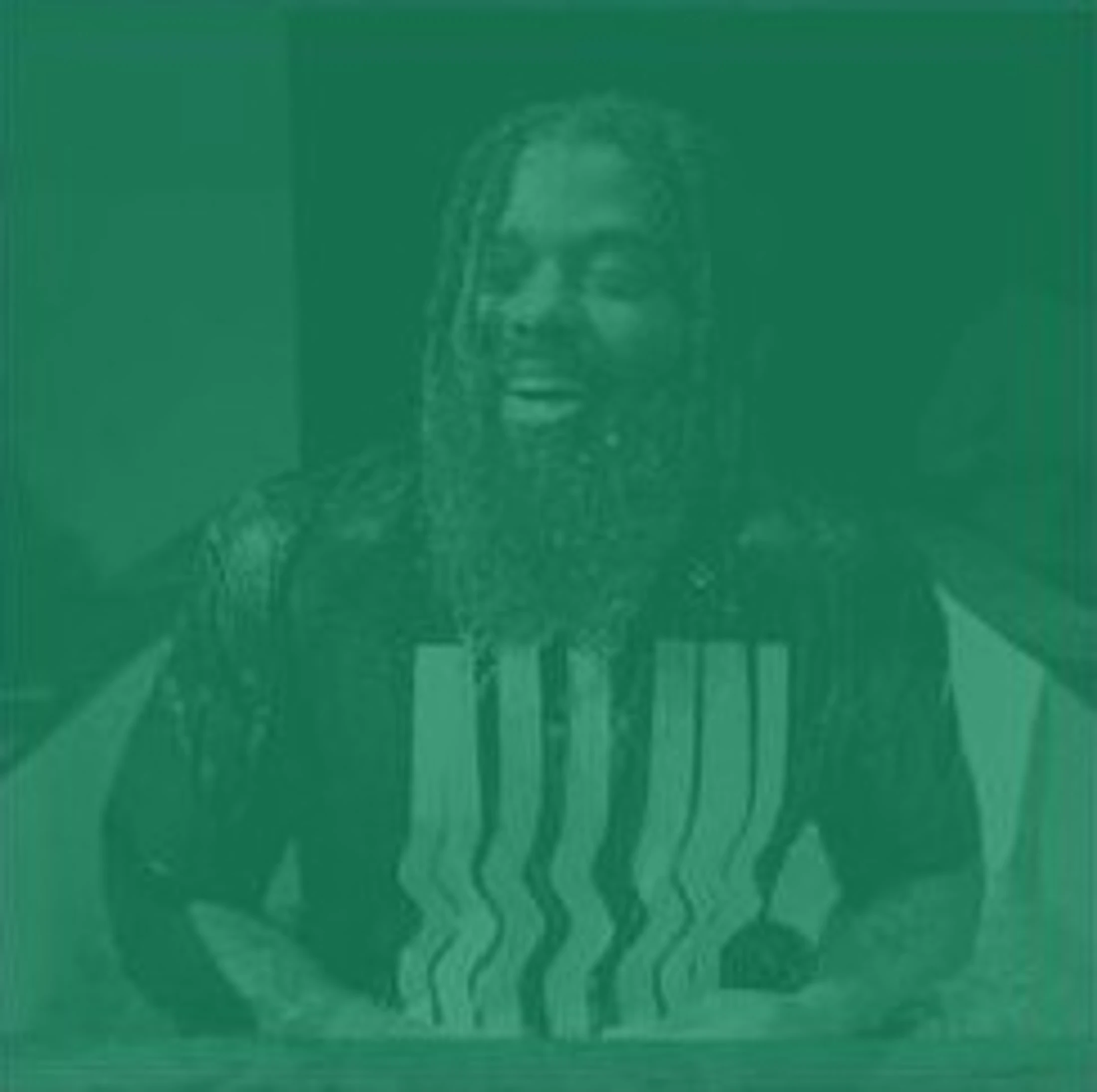 A green-toned, waist-up photo of a man with a long beard and dreadlocks sitting in what appears to be an ice bath, looking up with his mouth open.
