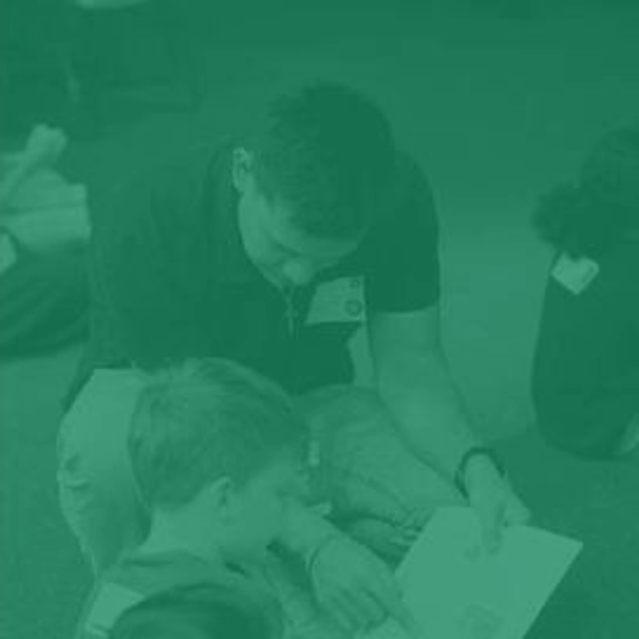 A green-tinted image of a young man kneeling to help a small boy read a piece of paper, pointing to something on the page.