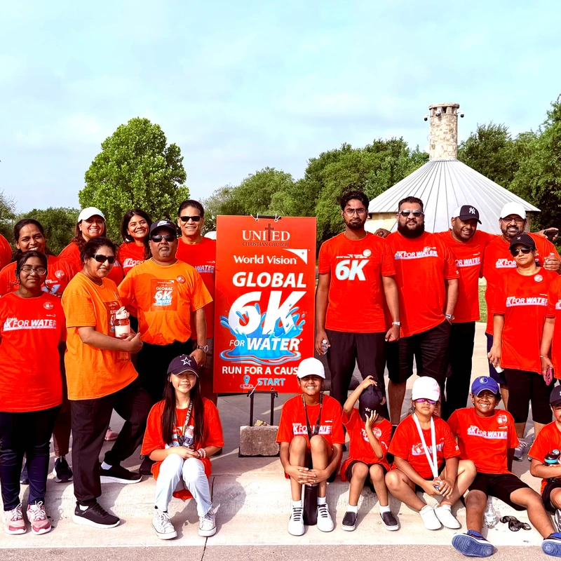 A large group of adults and children in matching orange t-shirts pose for a photo outdoors at the Global 6K for Water charity run.