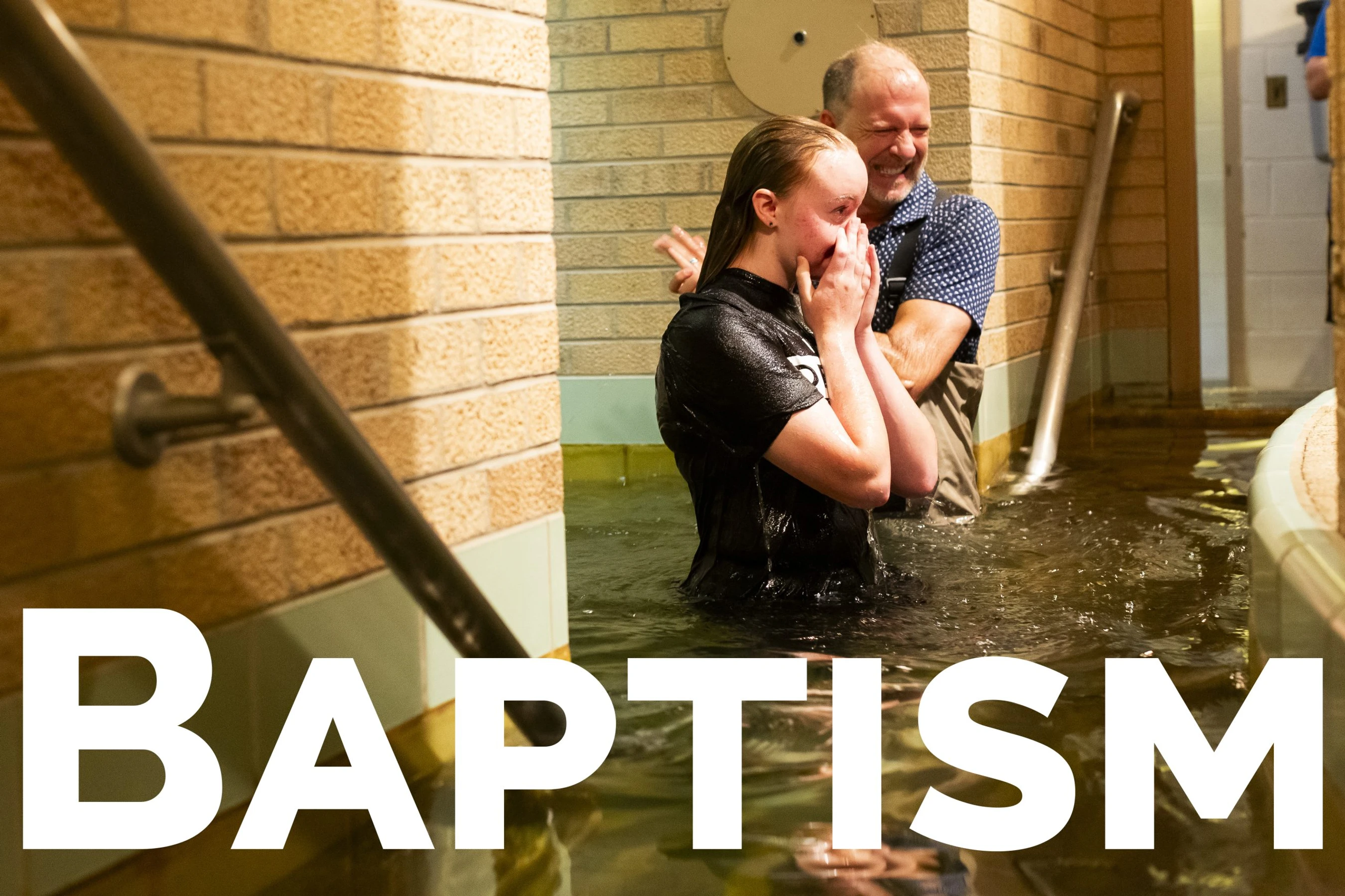 A young woman in a baptismal pool covers her face emotionally as a smiling man stands behind her. The word BAPTISM is written in large white letters.