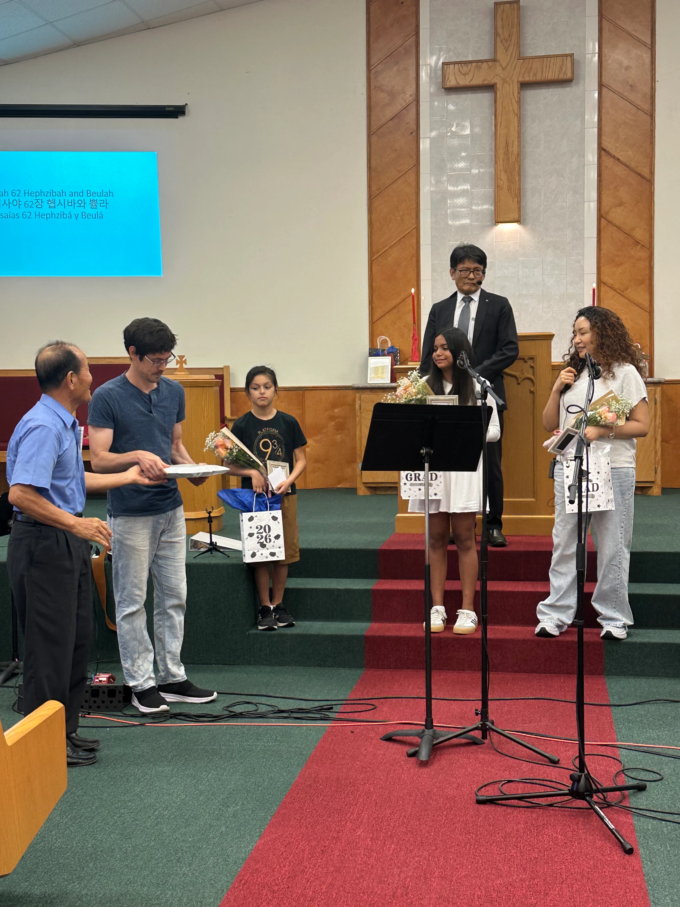 A group of students on a church stage being recognized for graduation, receiving certificates and gifts in front of the congregation.