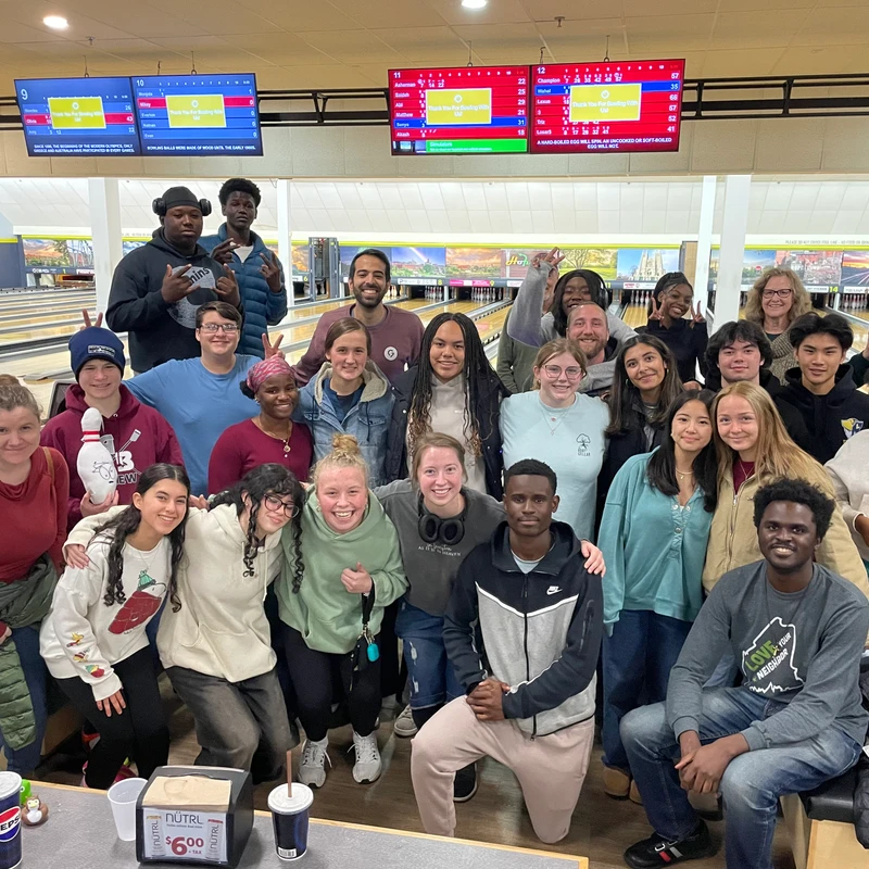 A large, diverse group of smiling people of various ages poses together for a picture inside a brightly lit bowling alley.