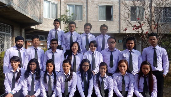 A group of male and female students in matching purple shirts and dark ties pose for a formal portrait outdoors in front of a brick building.