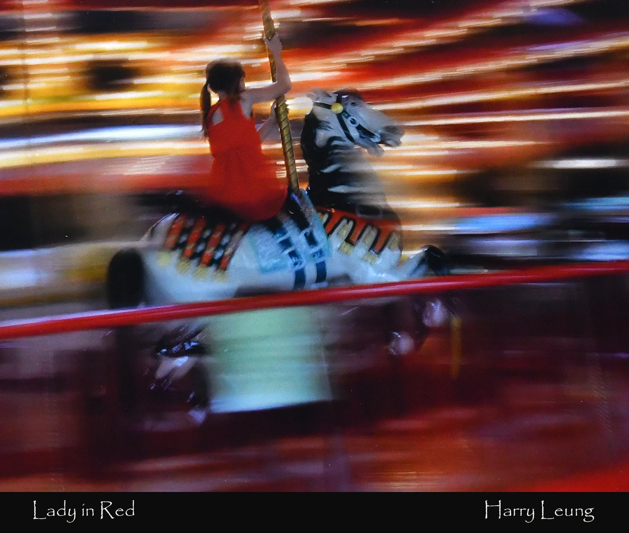 A motion-blurred photograph of a girl in a red dress riding a carousel horse, with a background of streaking red, orange, and yellow lights.