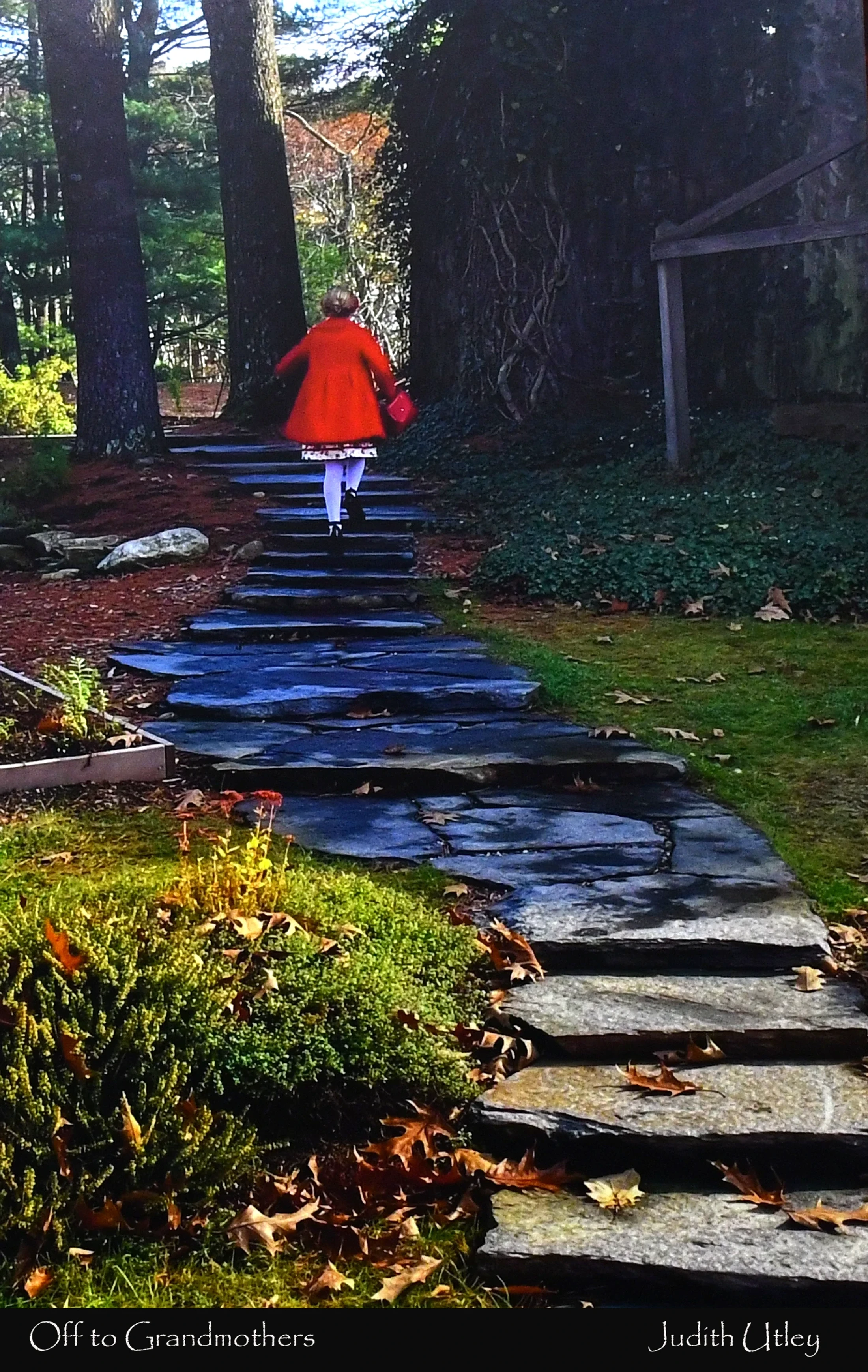 A person in a bright red coat, resembling Little Red Riding Hood, walks up a winding stone path through a wooded garden in autumn.