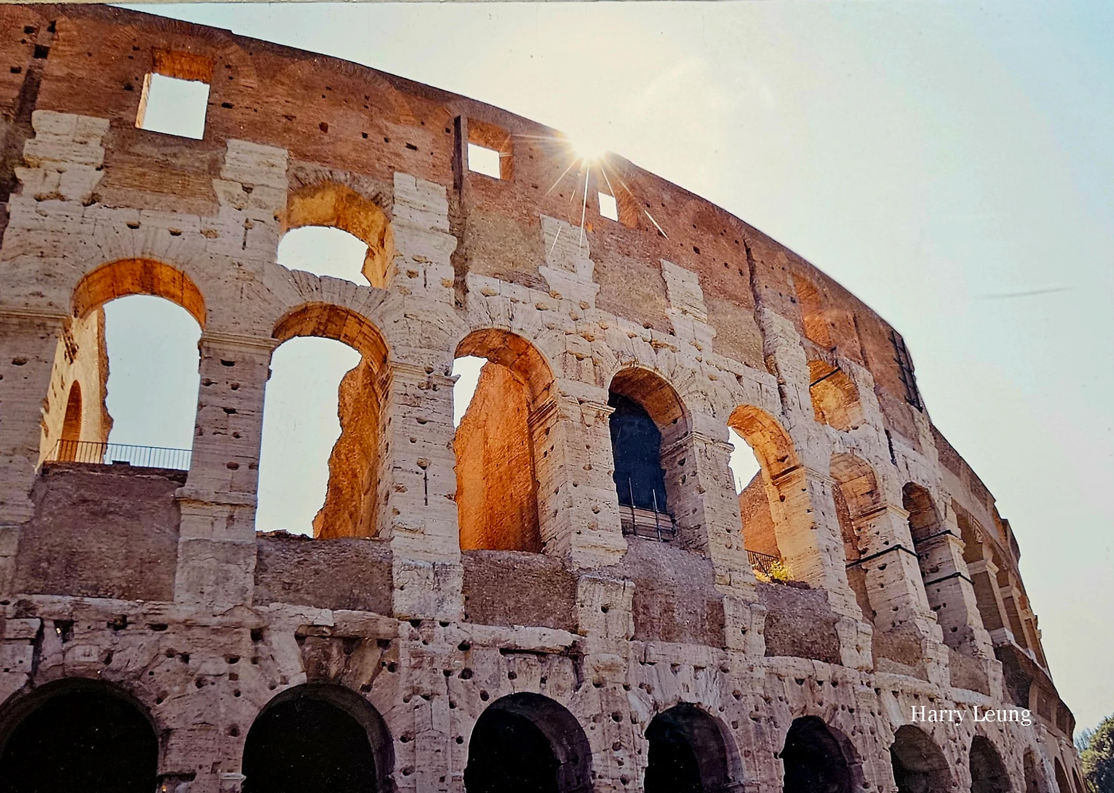 A low-angle shot of the sun bursting over the ancient, weathered stone walls of the Colosseum in Rome, highlighting its iconic arches.