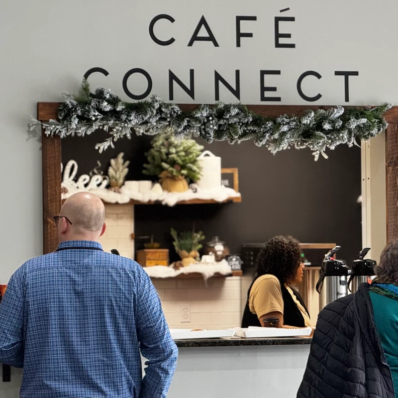 People gather around the Café Connect counter, which is decorated with a festive winter garland. A barista is visible serving customers.