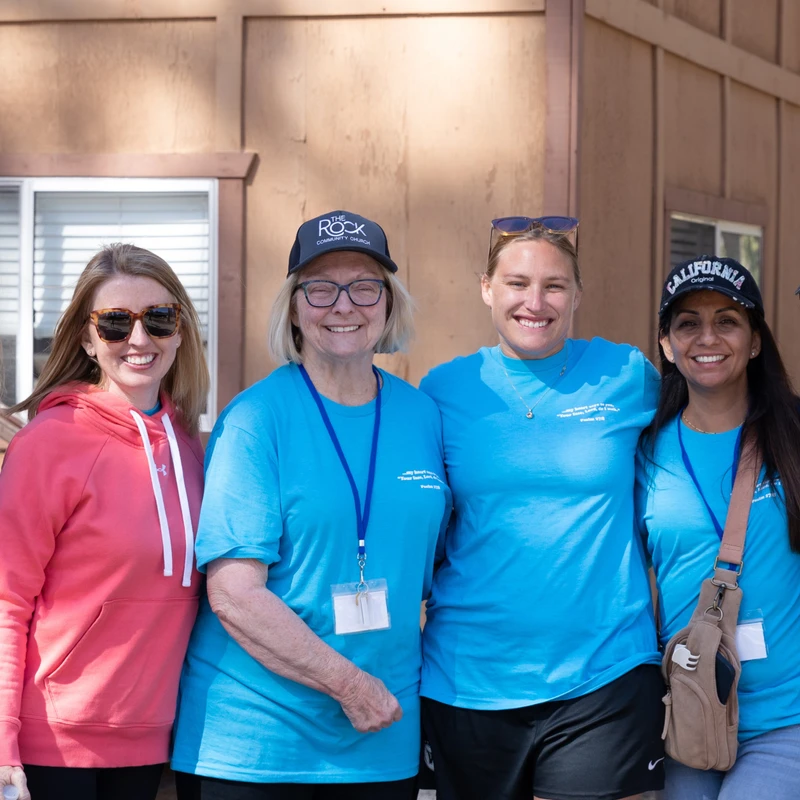 A group of six women pose for a photo in front of a wooden cabin. They are all smiling, and most are wearing matching bright blue t-shirts.