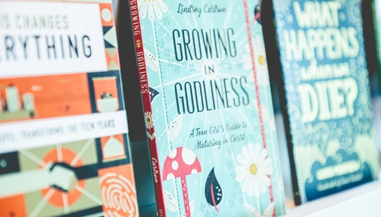 A close-up of Christian books on a shelf, with 'Growing in Godliness' by Lindsey Carlson in focus in the center.