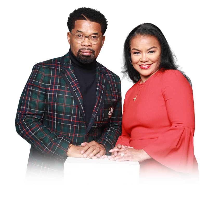 A portrait of a Black man and woman standing side-by-side. He wears a green plaid blazer and glasses, and she wears a bright red dress and smiles.
