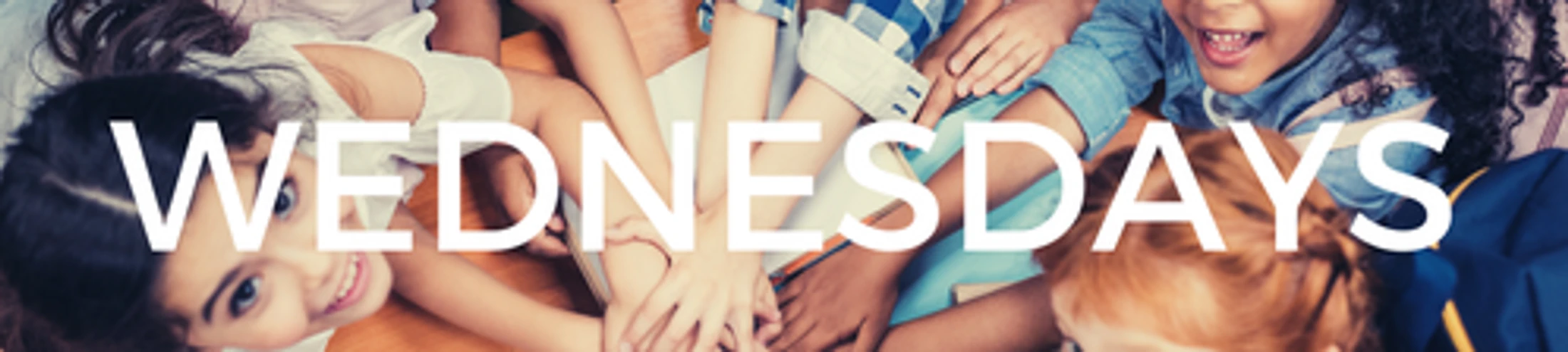 A top-down view of a diverse group of children in a huddle with their hands together, with the word 'WEDNESDAYS' in white text over the image.