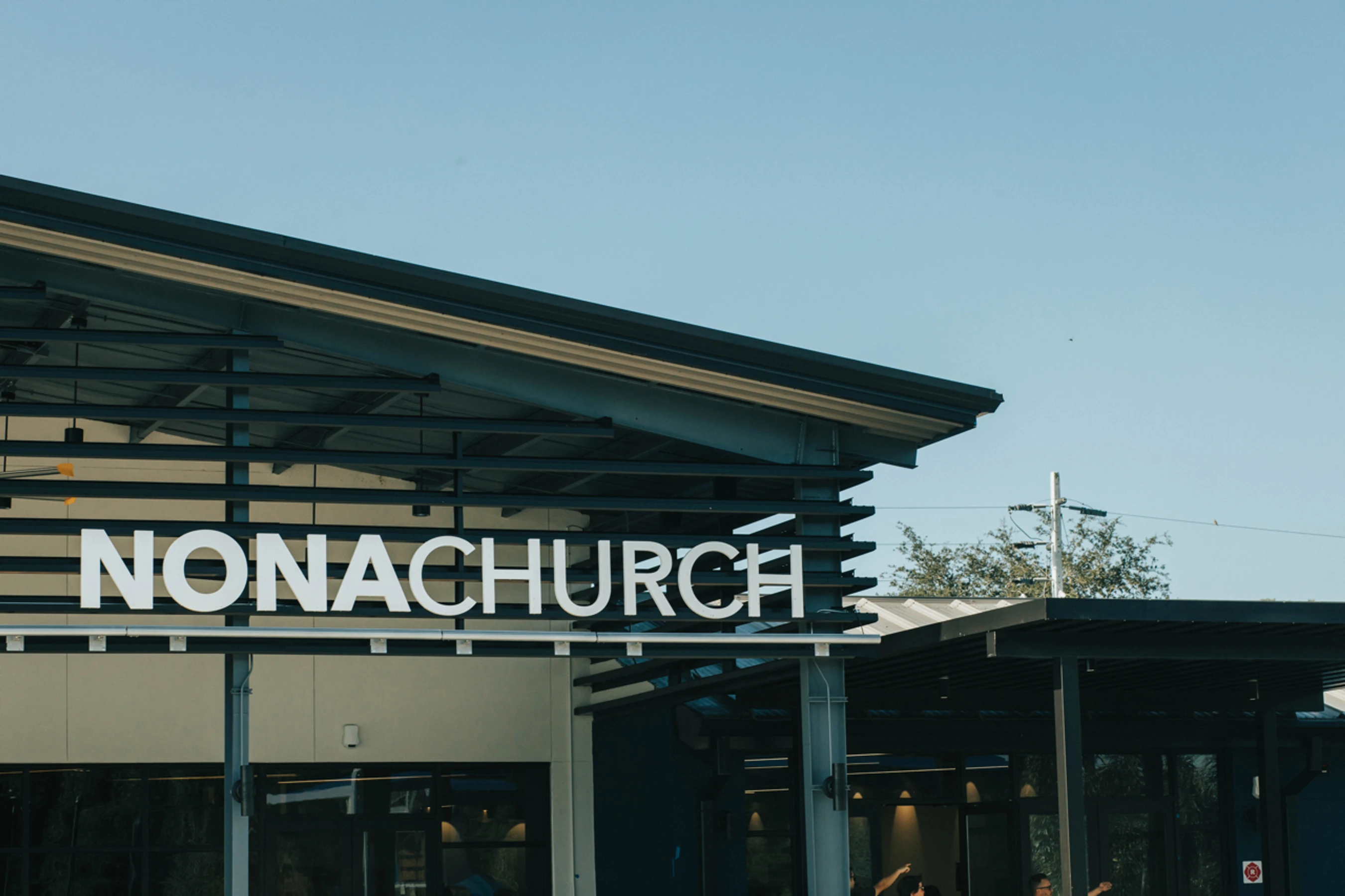 A large white sign reading 'NONACHURCH' is mounted on the modern exterior of a building with a dark metal roof against a clear blue sky.