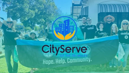 A group of smiling CityServe volunteers, adults and children, hold a large banner that reads 'Hope. Help. Community.' at an outdoor event.