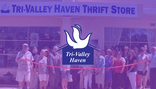 A large group of people poses for a photo during a ribbon-cutting ceremony in front of the Tri-Valley Haven Thrift Store, with a purple overlay.