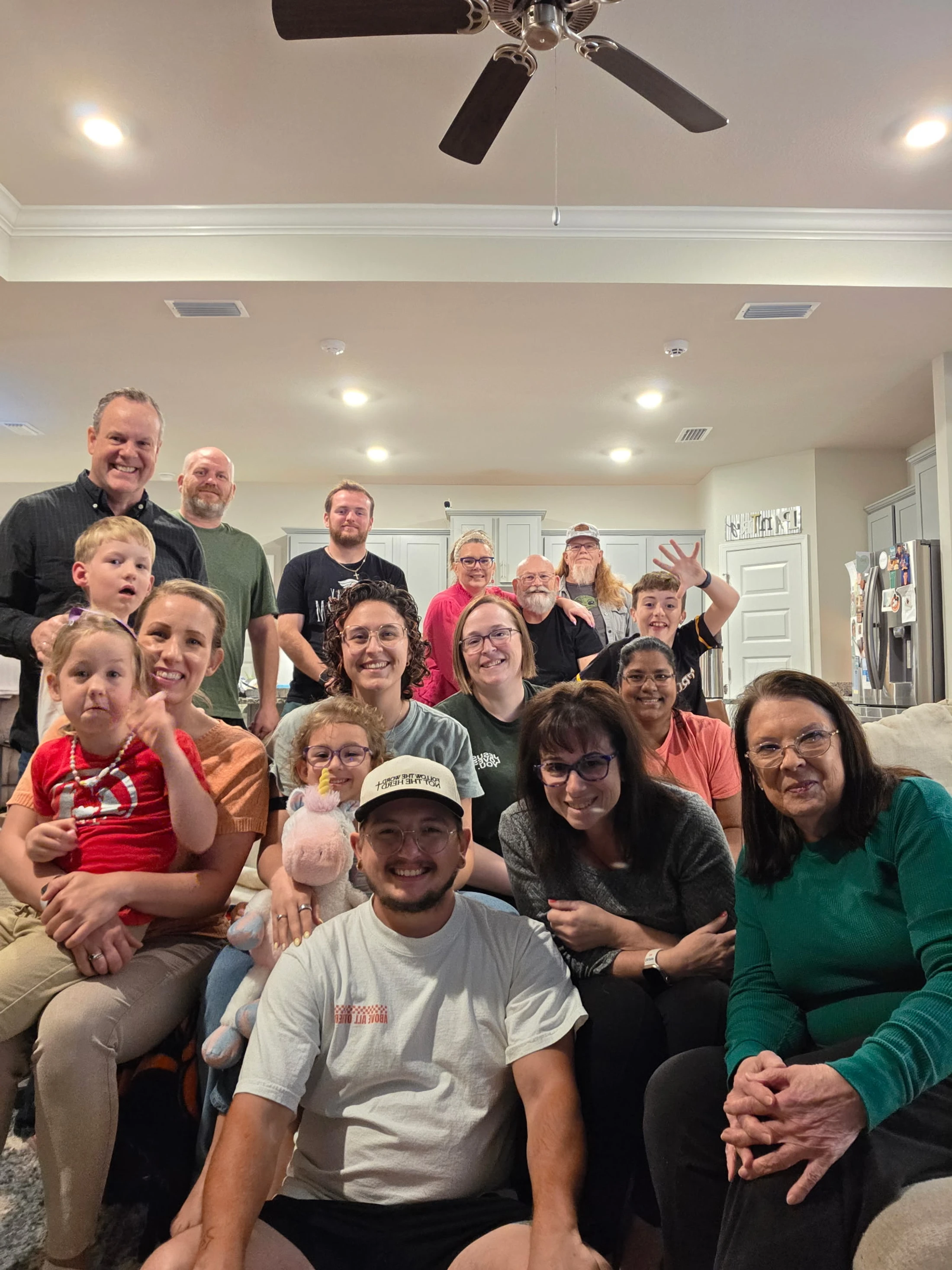 A large group of smiling people of all ages posing for a happy photo together in a home's living room, gathered on and around a couch.