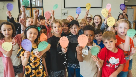 A large, diverse group of smiling children hold up colorful paper balloons with the words 'I Love My Church' written on them.