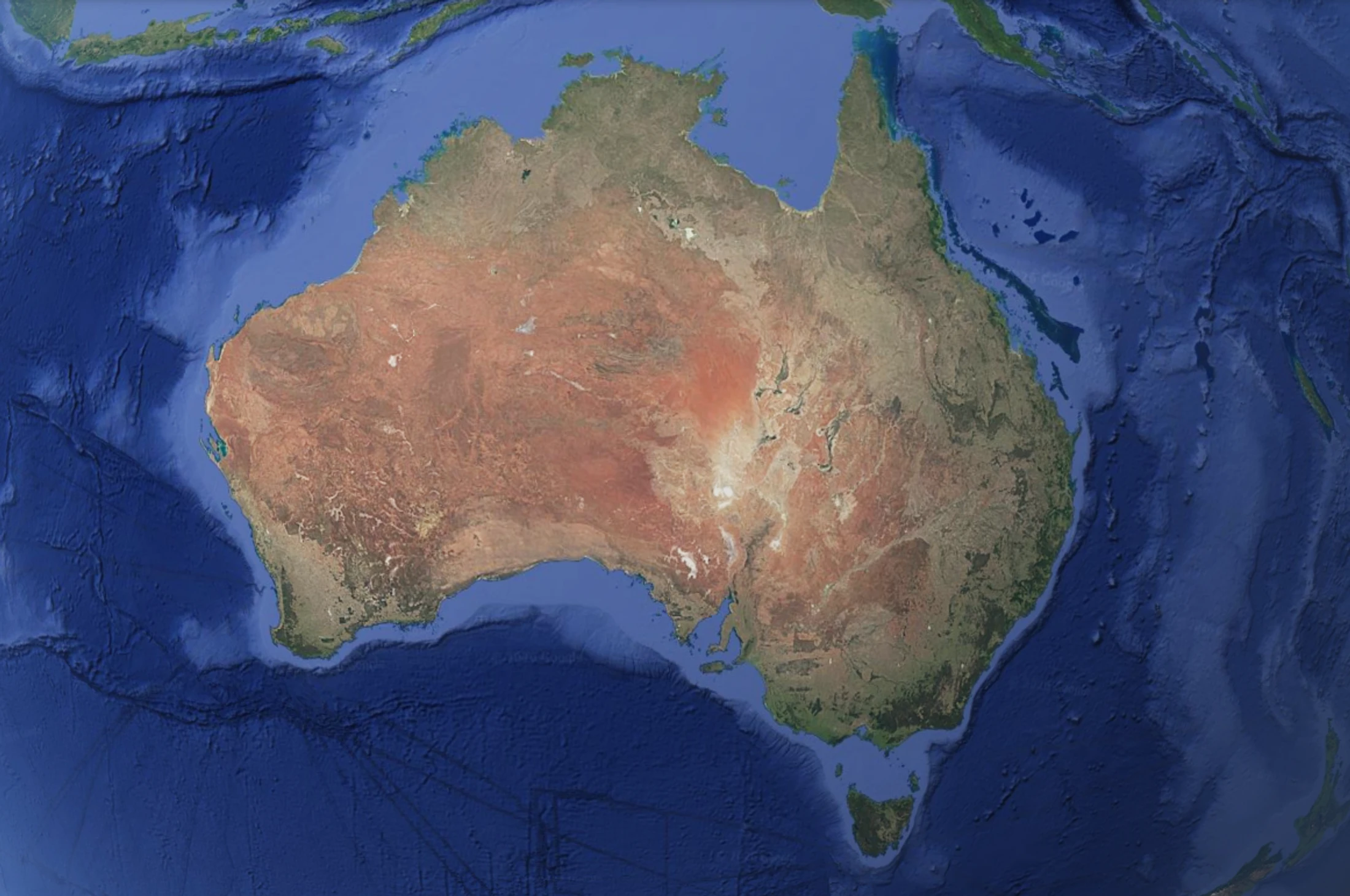 A satellite image of Australia, showing its reddish-brown outback center and greener coastal regions, surrounded by the deep blue of the surrounding oceans.