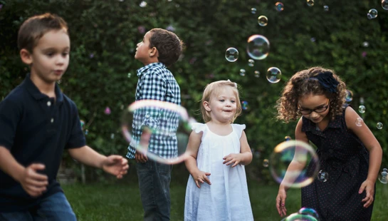 Four children playing with floating bubbles in a green garden