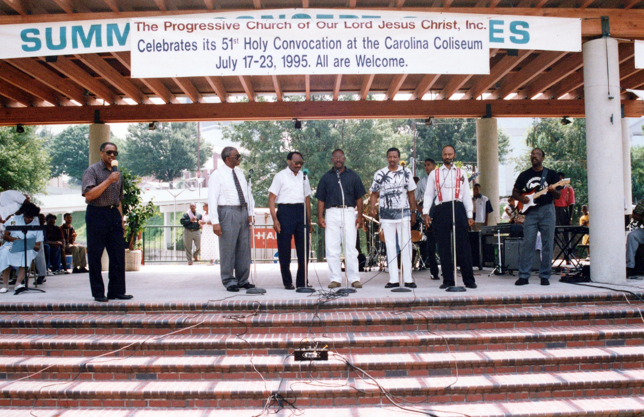 A group of Black men perform on an outdoor stage under a banner for the Progressive Church's 51st Holy Convocation in July 1995.