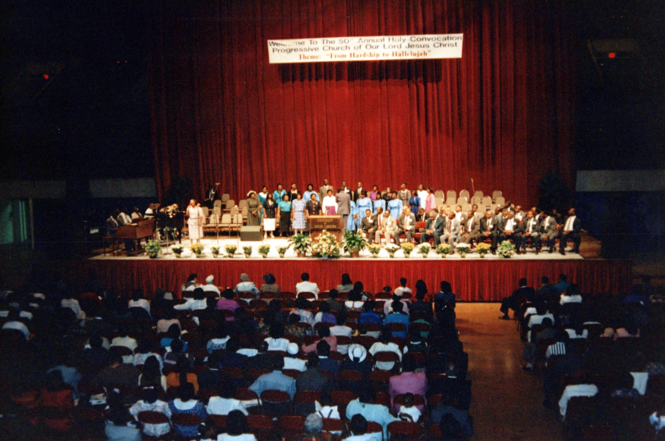 An audience watches a large group on stage during the 50th Annual Holy Convocation of the Progressive Church of Our Lord Jesus Christ in an auditorium.