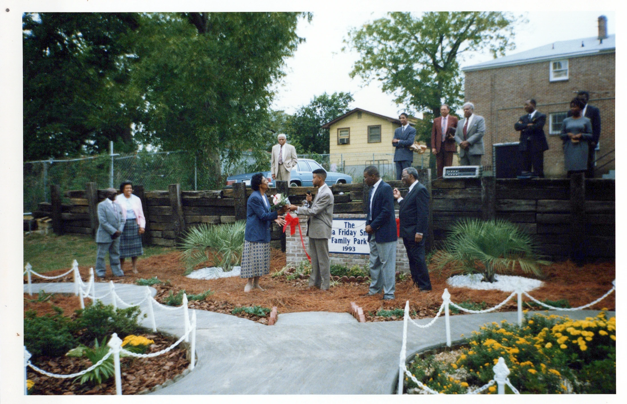 A group of African American men and women at the 1993 dedication of a family park. A man in a suit presents a woman with a bouquet of flowers.