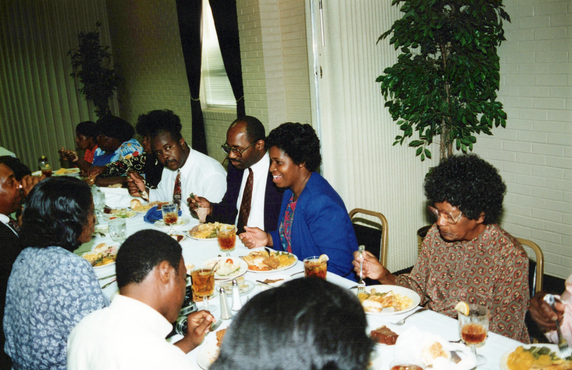 A vintage photograph of African American men and women sitting at a long table, eating and socializing during a formal dinner or banquet.