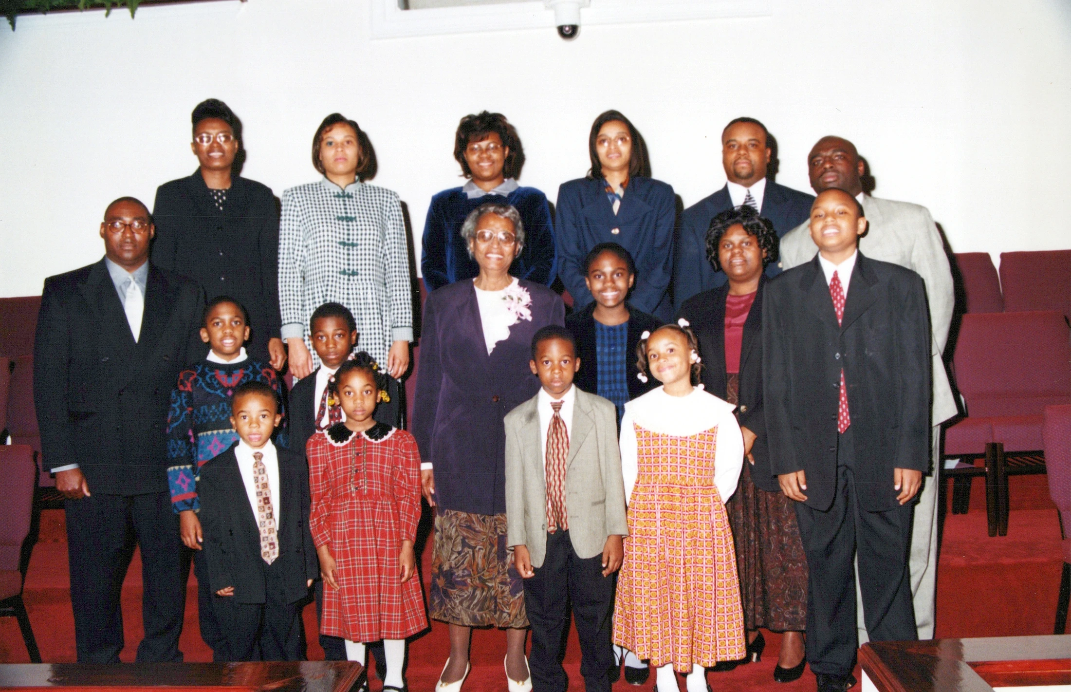 A large, multi-generational African American family poses for a formal group portrait inside a church, all dressed in their Sunday best.