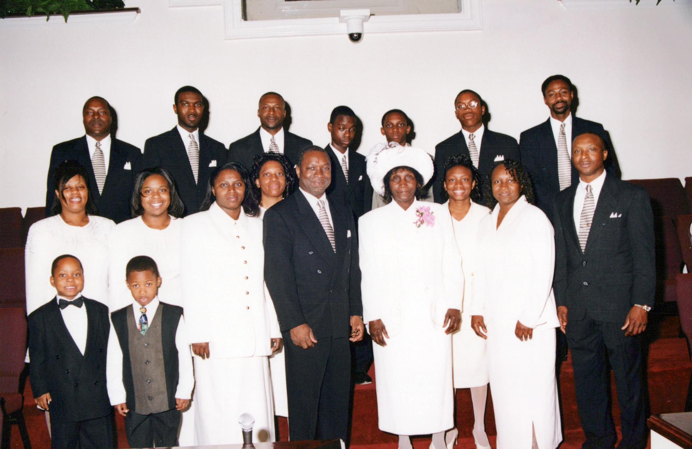 A large group of Black men, women, and boys posing for a formal portrait inside a church. The men wear dark suits and the women wear mostly white outfits.