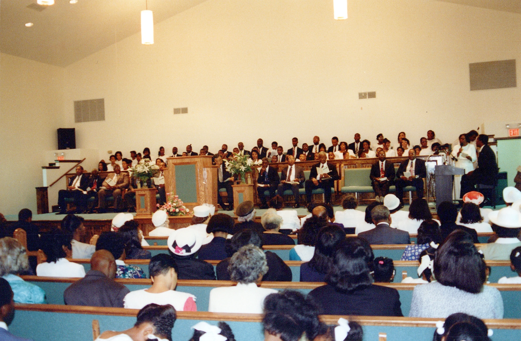 A wide shot from the back of a church showing a large African American congregation sitting in pews and listening to a service.