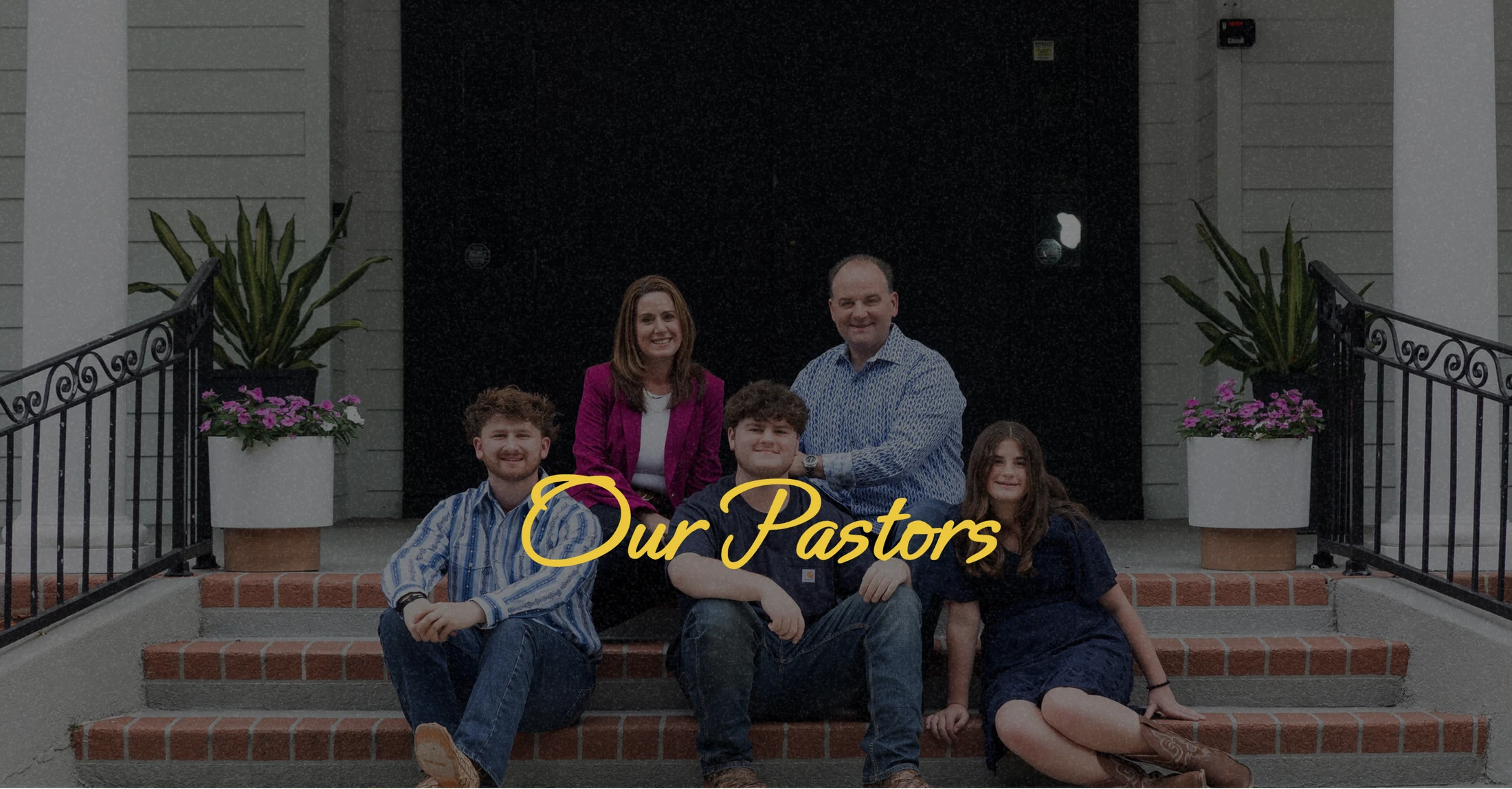 A family of five, the pastors and their three children, smiling for a group portrait while sitting on the brick steps of a building.