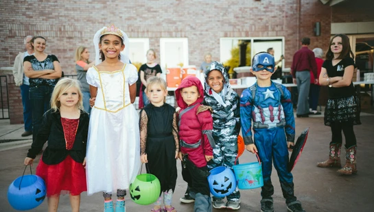 children standing while holding Jack 'o lantern and wearing costume