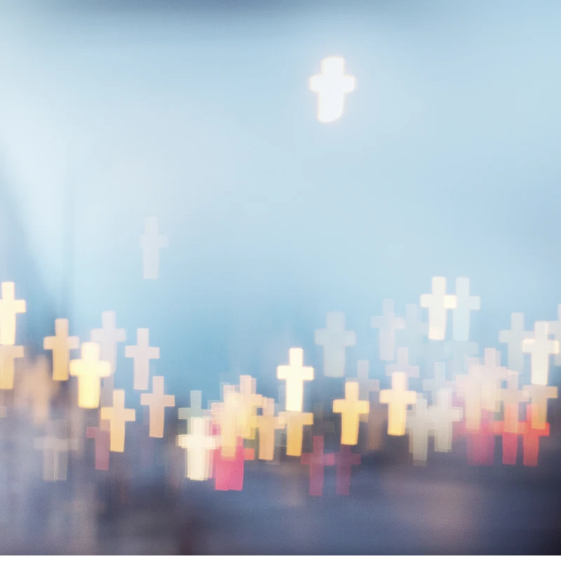 An abstract photo with soft, out-of-focus lights shaped like crosses in yellow, white, and red, floating against a dreamy, soft blue background.