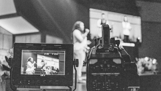 greyscale photography of video camera capturing person standing on stage