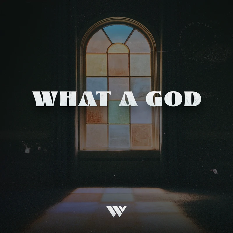 The words 'What a God' are overlaid on a dark room with light shining through a colorful, arched stained-glass window, creating a reflection on the floor.