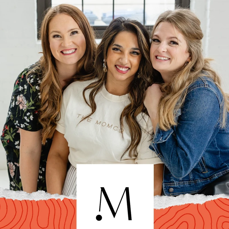 Three diverse women pose together, smiling at the camera. The woman in the middle wears a cream t-shirt with 'THE MOMCO' on it. A logo is at the bottom.