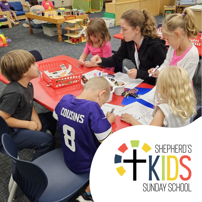 A group of young children and a teacher sit at a red table in a classroom, coloring and doing crafts during Shepherd's Kids Sunday School.