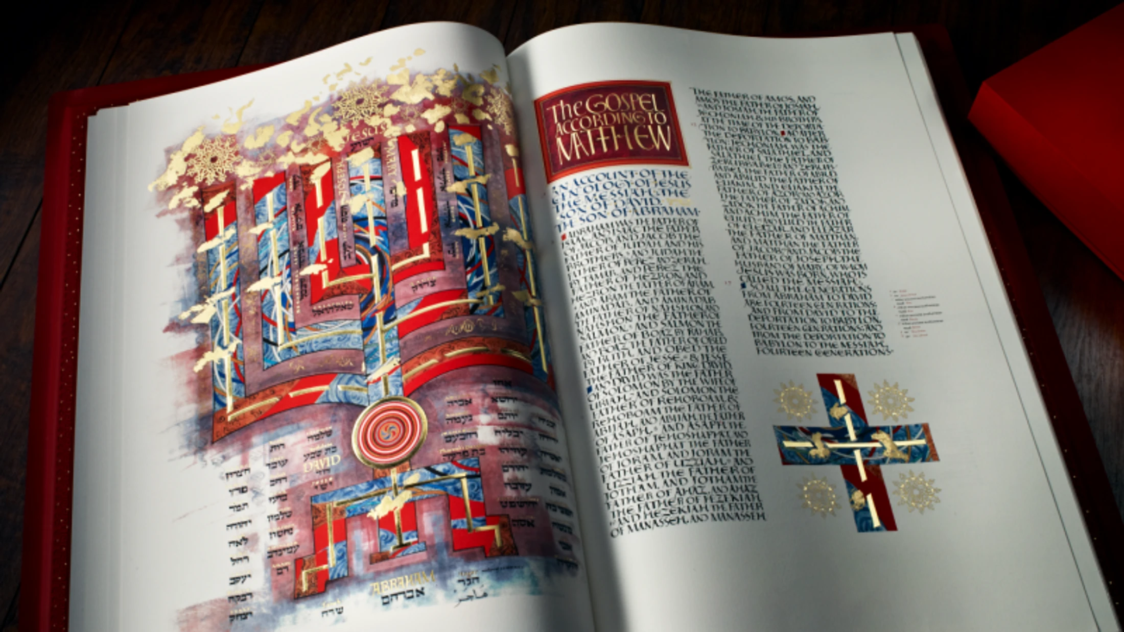 An open book with a red cover displays the Gospel of Matthew. The pages are decorated with calligraphy, gold leaf, and an intricate, colorful illustration.