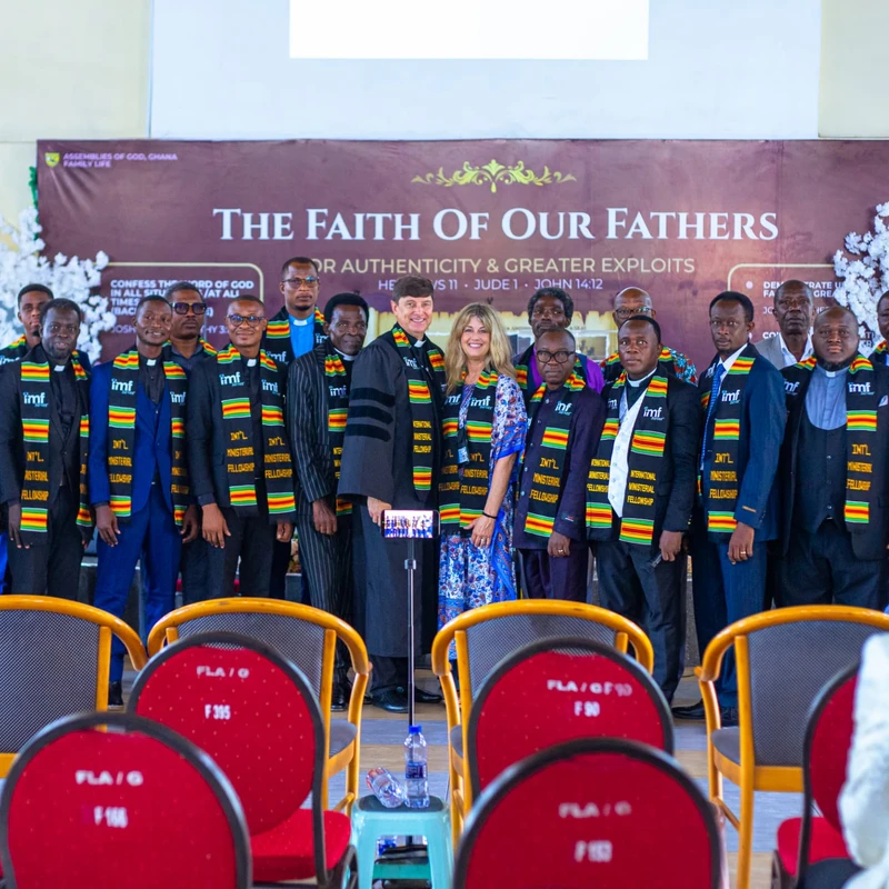 A large, diverse group of ministers pose on a stage in front of a banner that reads "The Faith Of Our Fathers" during a conference in Ghana.