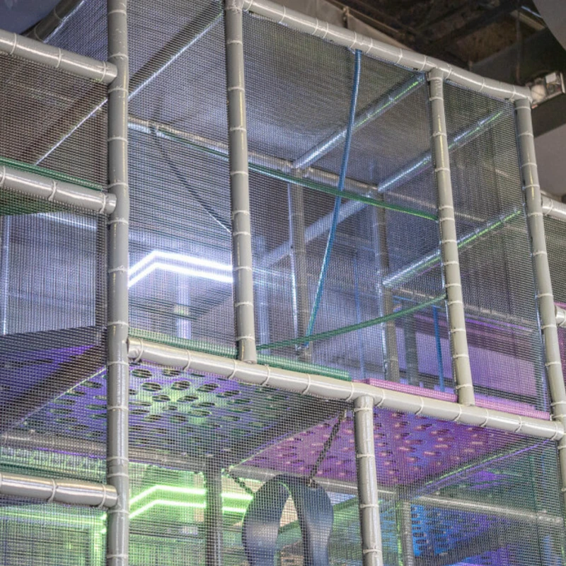 A multi-level indoor jungle gym with gray padded poles and safety netting, illuminated by bright green, purple, and white LED strip lights.