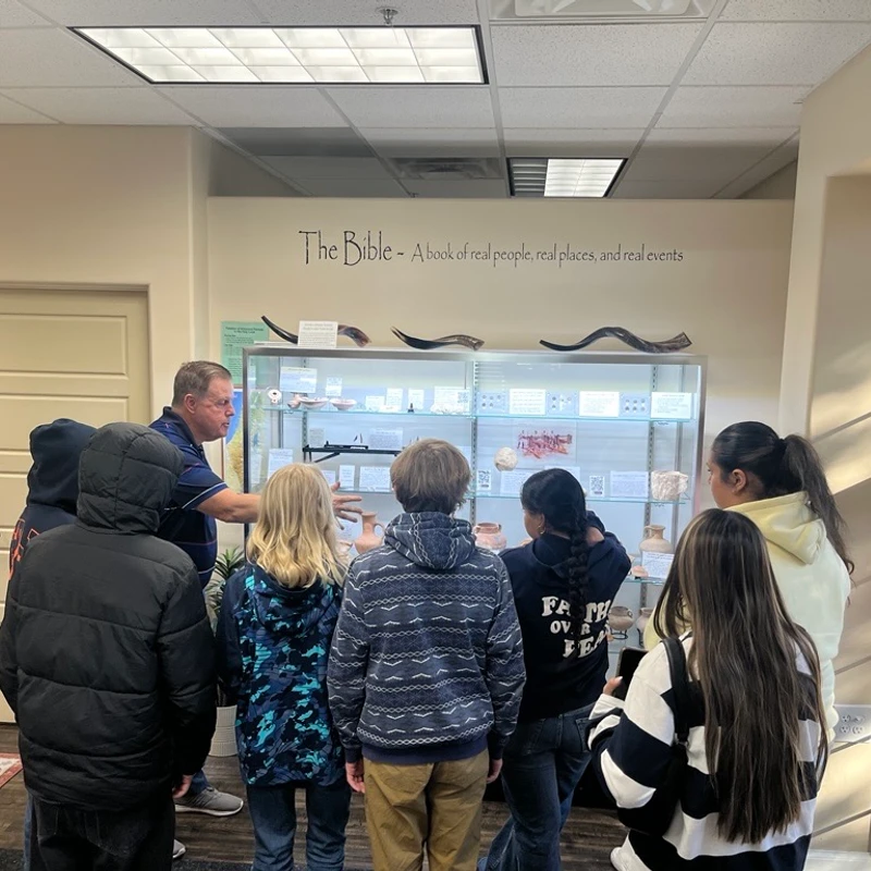 A tour guide shows a group of young students artifacts in a glass display case at a museum exhibit about the Bible.