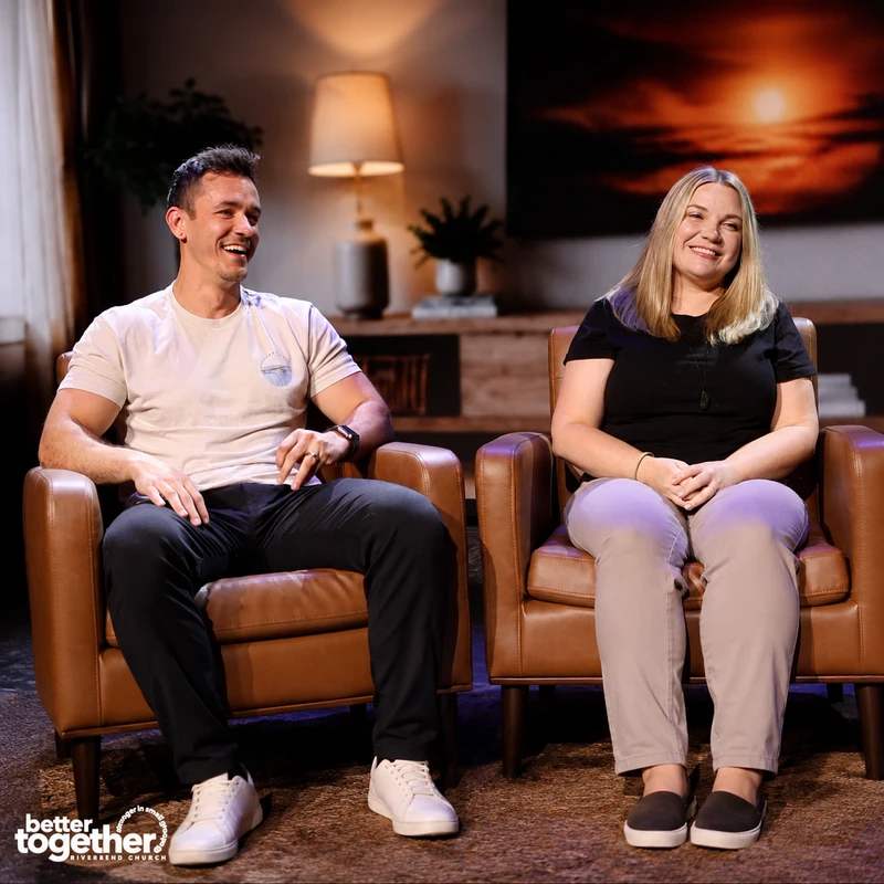 A smiling man and woman sit in brown leather armchairs on a stage for a 'Better Together' church event. The man laughs while the woman smiles warmly.