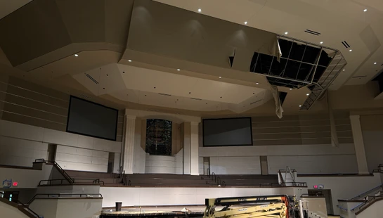 Interior of a large church sanctuary during construction, with a boom lift on the floor and a large hole in the damaged ceiling above the stage.
