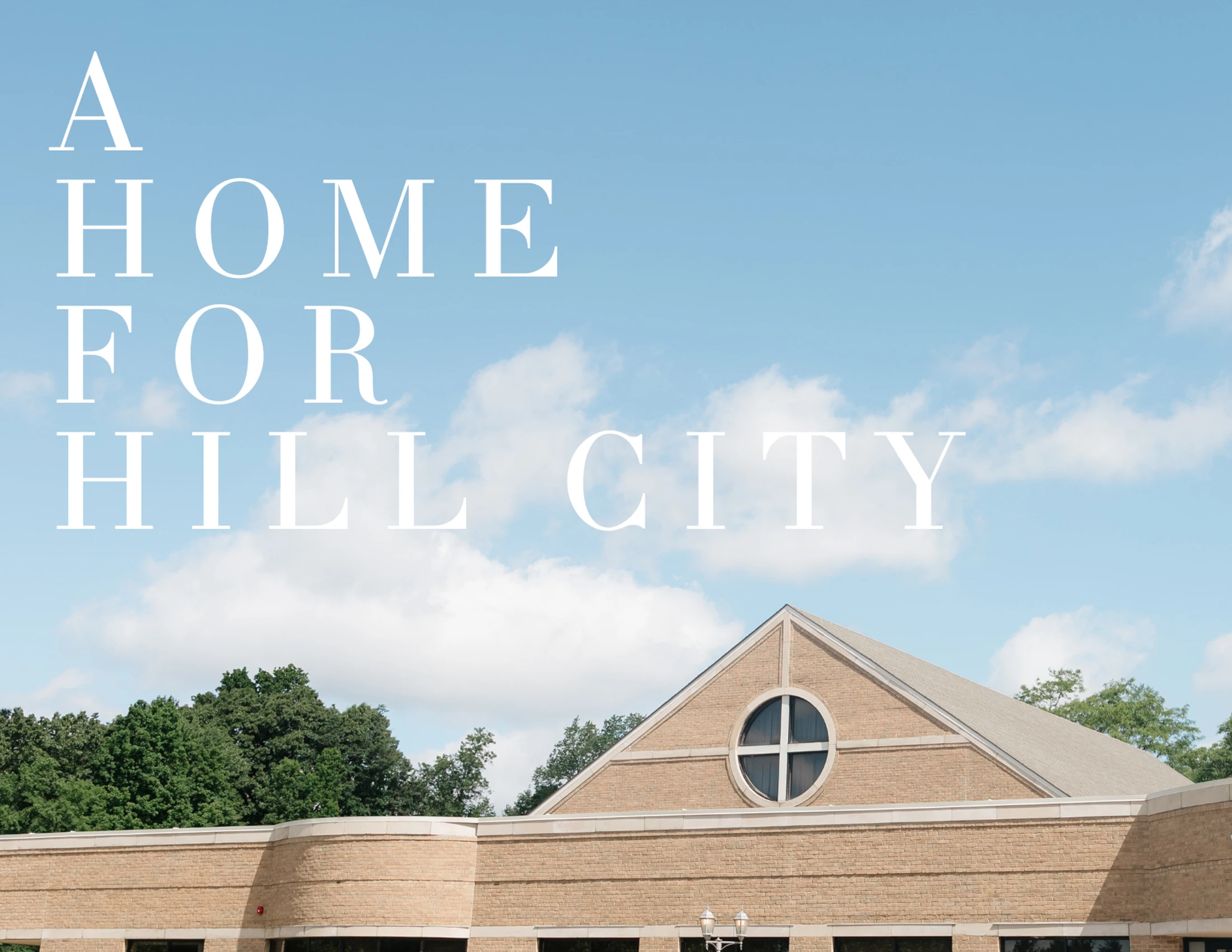 A light brown brick building with a gabled roof and a circular window is shown against a blue sky with clouds. White text reads 'A HOME FOR HILL CITY'.
