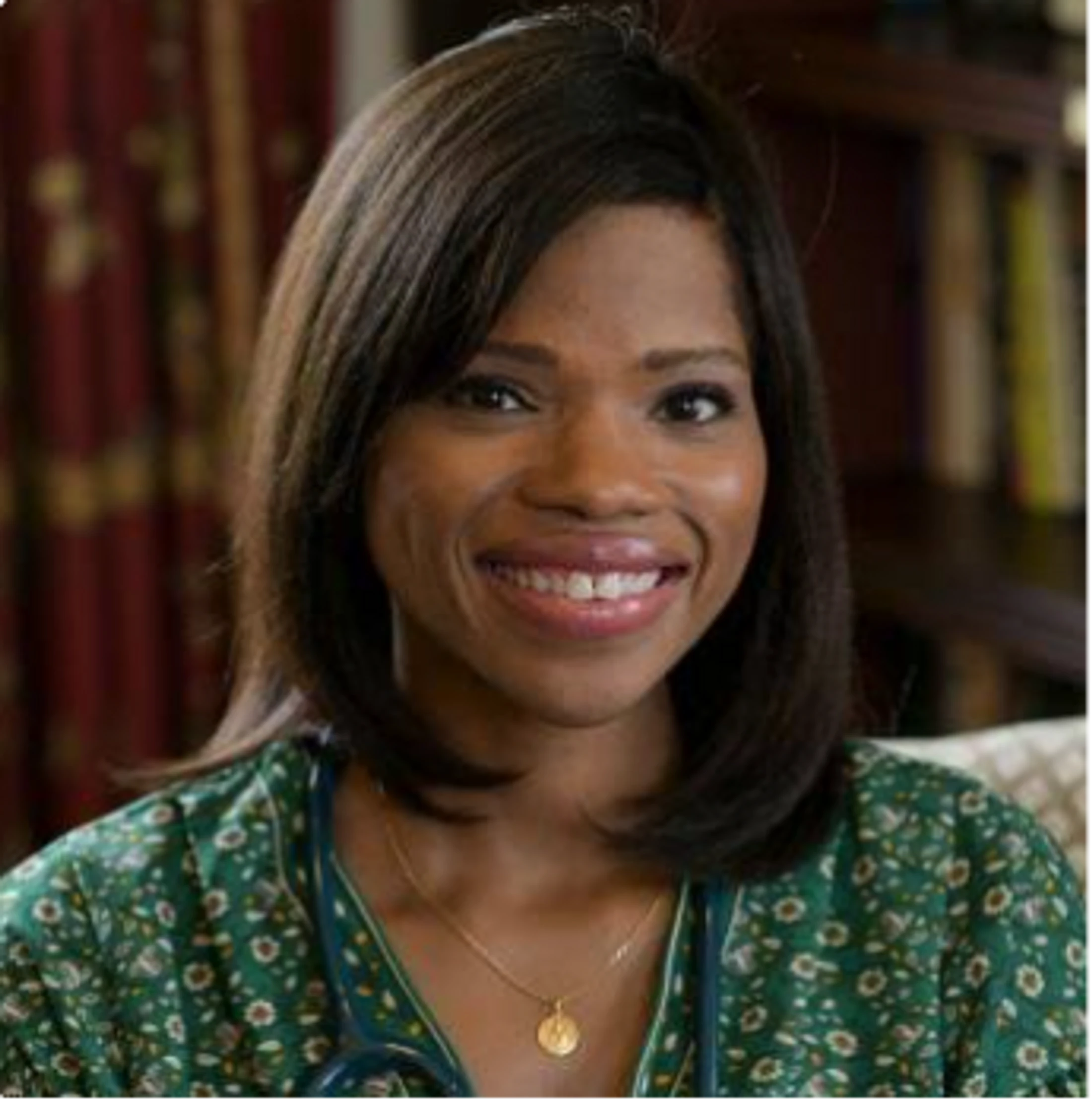 A headshot of a smiling Black woman with shoulder-length dark hair, wearing a green patterned shirt and a stethoscope around her neck.