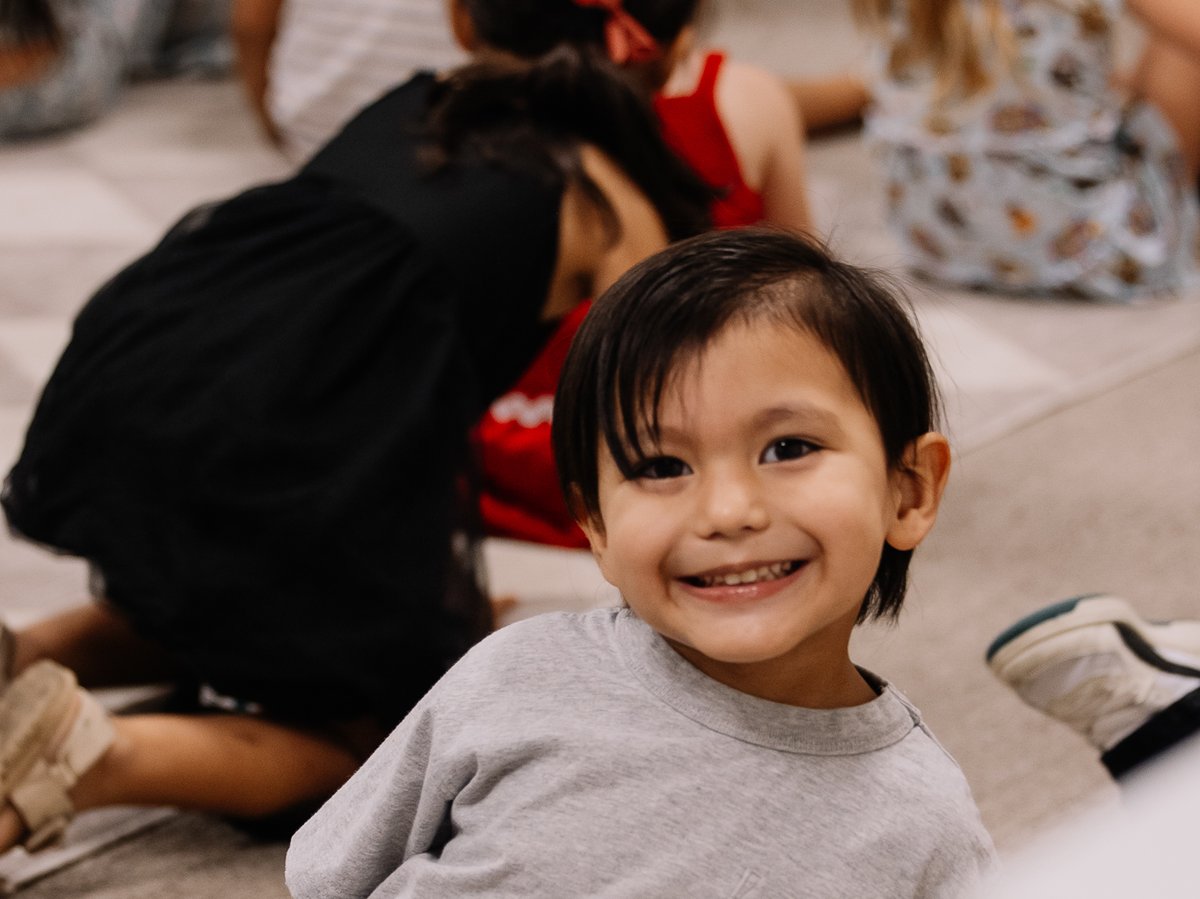 A smiling Branches-age boy sitting with his class at Discovery Kids