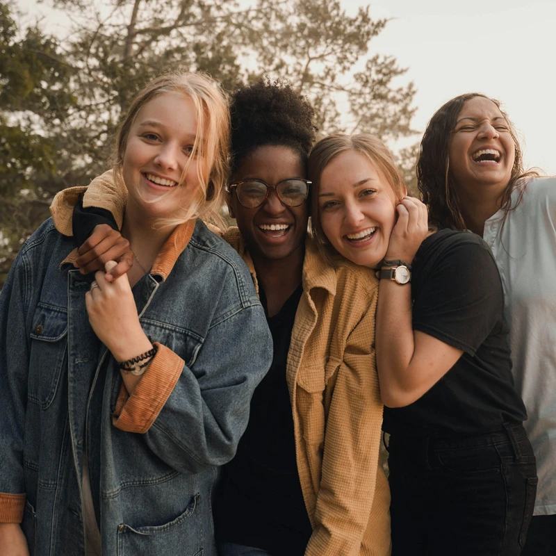 Four women laughing together in a line outdoors during the golden hour